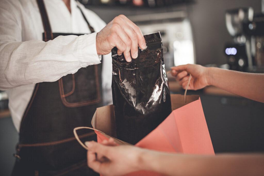 Professionelle Barista geben Kaffee Packung in Einkaufstasche